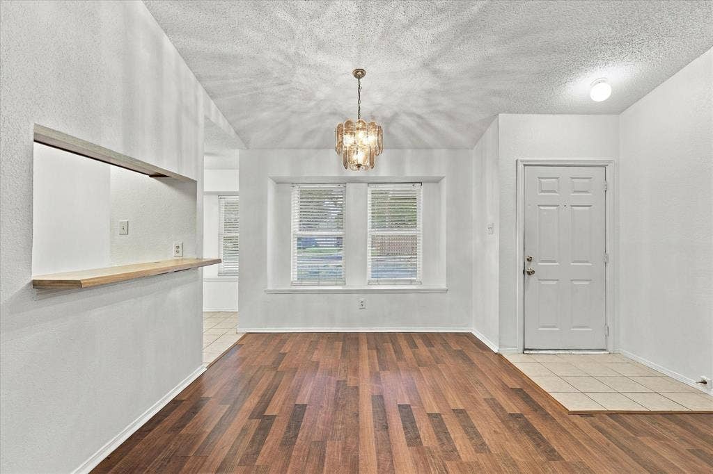 844 Woodrock Drive, Dallas, TX 75217 Vaulted ceiling, wood-finish flooring, pass-through window with wood counter, decorative chandelier, and paneled entry door with tile flooring
