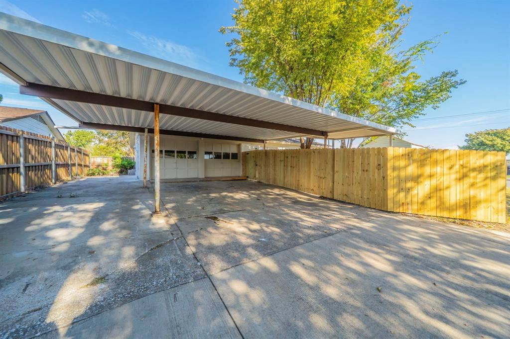 802 Birchwood Drive, Garland, TX 75043 Carport with corrugated metal roofing, concrete driveway, wood privacy fencing, and an attached garage with panel doors