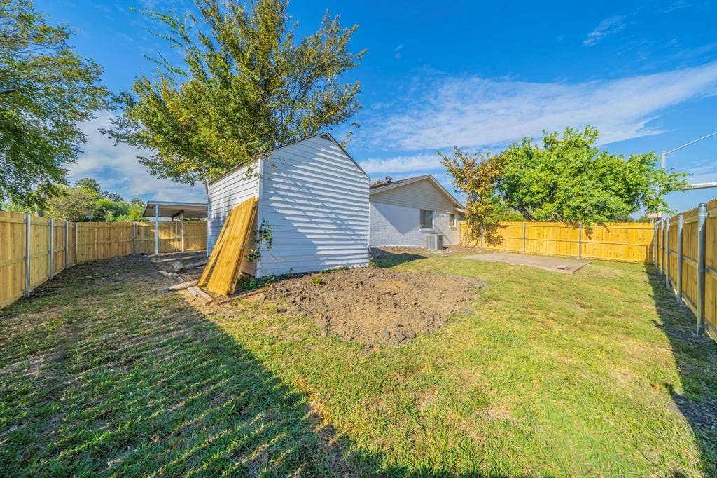 802 Birchwood Drive, Garland, TX 75043 Expansive fenced backyard with a detached storage shed, lush green lawn, and mature trees