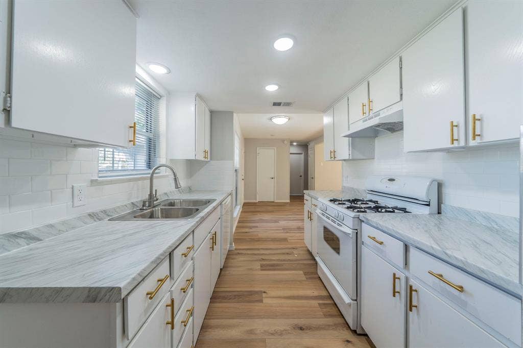 802 Birchwood Drive, Garland, TX 75043 White cabinetry with gold-tone hardware, wood-finish flooring, white subway tile backsplash, and light-toned countertops