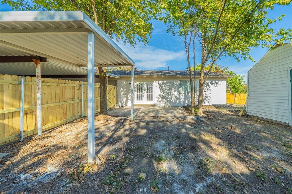 802 Birchwood Drive, Garland, TX 75043 Covered carport structure, wood privacy fencing, white exterior siding, rear patio area, and exterior storage building