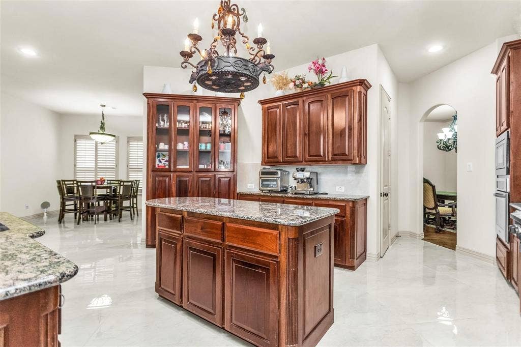 1838 Olney Drive, Allen, TX 75013 Kitchen featuring a central island with a stone countertop, rich wood-finish cabinetry, and polished tile flooring