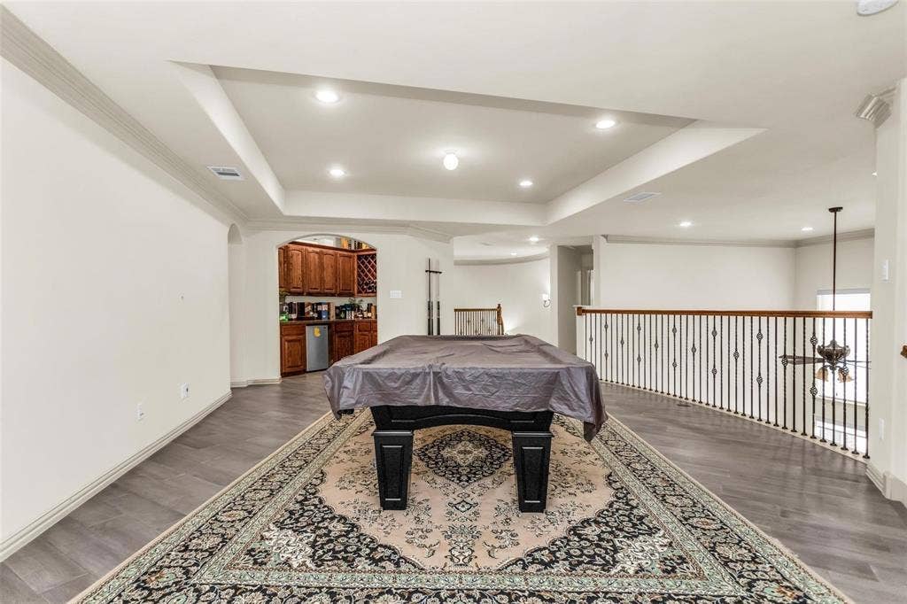 1838 Olney Drive, Allen, TX 75013 Tray ceiling with recessed lighting, wood-finish flooring, built-in wet bar with wood cabinetry, and wrought iron railing