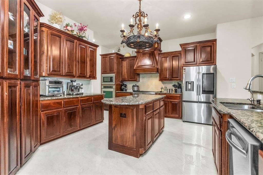 1838 Olney Drive, Allen, TX 75013 Kitchen featuring extensive wood cabinetry, granite countertops, stainless steel appliances, a center island, and a decorative chandelier