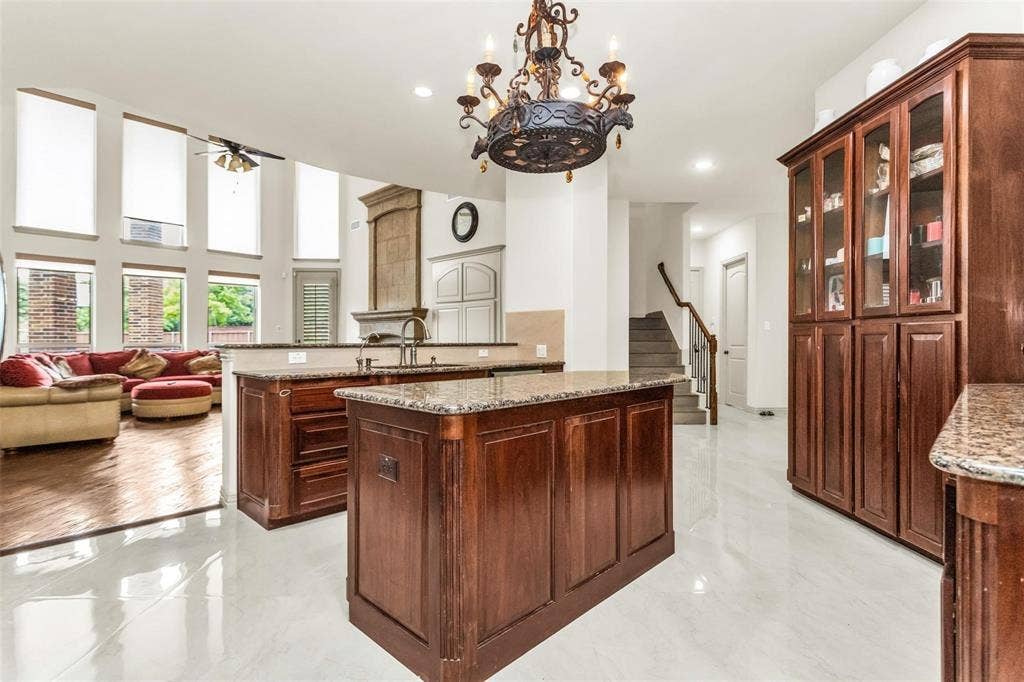 1838 Olney Drive, Allen, TX 75013 Central kitchen islands with granite countertops, rich wood cabinetry with glass-front display, white tile flooring, and high ceilings with upper windows