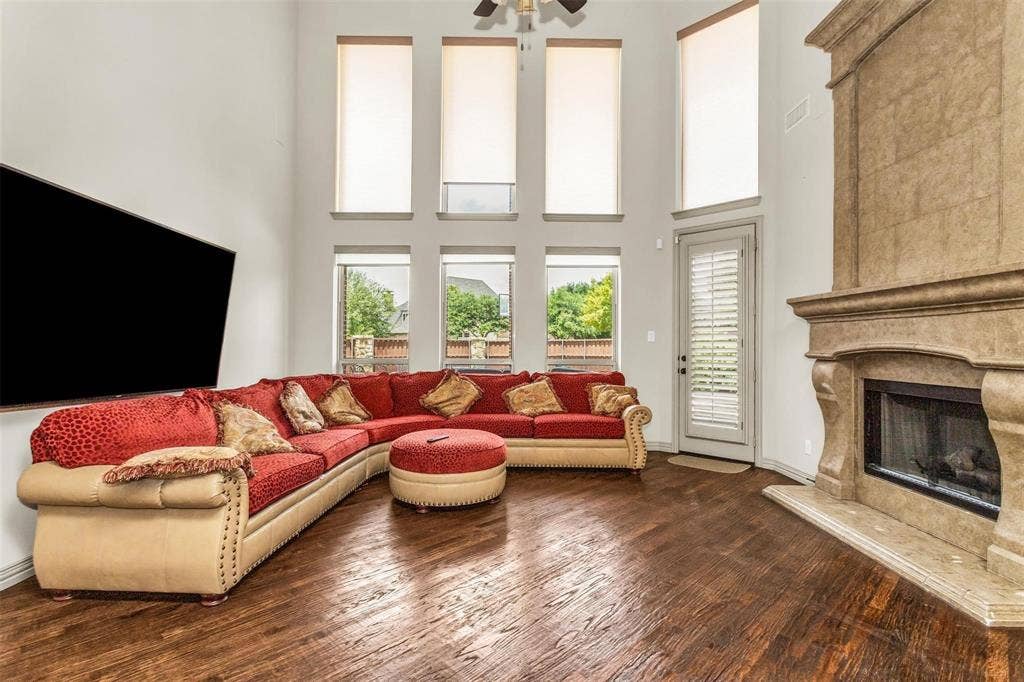 1838 Olney Drive, Allen, TX 75013 Two-story living area featuring wood-finish flooring, a stone-clad fireplace, and multiple windows with roller shades