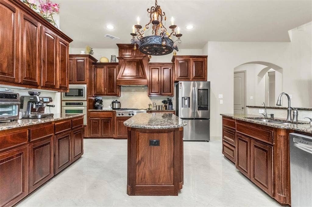 1838 Olney Drive, Allen, TX 75013 Expansive kitchen with wood cabinetry, granite countertops, stainless steel appliances, a kitchen island, and archway details