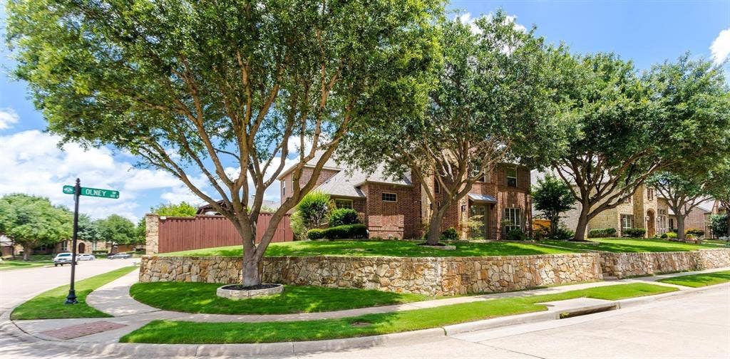 1838 Olney Drive, Allen, TX 75013 Corner lot featuring mature trees, a stone retaining wall, and manicured landscaping