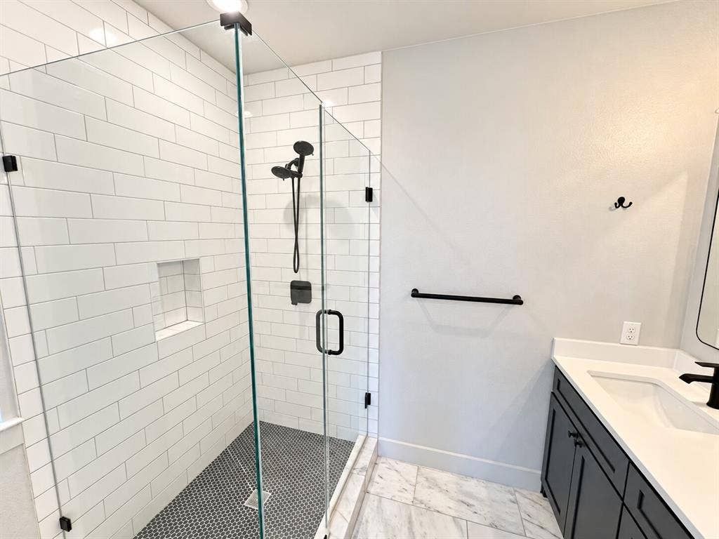 Glass-enclosed shower with white subway tile surround and black penny tile flooring, featuring a built-in shower niche and matte black fixtures
