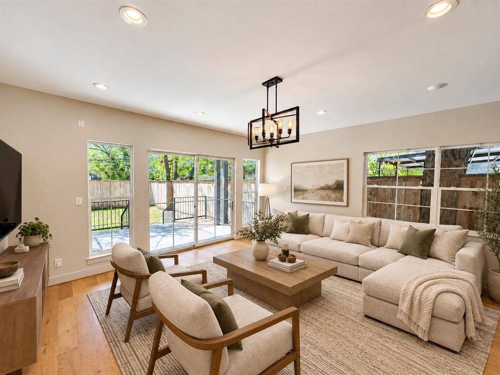 Virtually staged -Bright, light-filled living room featuring multiple glass doors and windows with wood-finish flooring, recessed ceiling lighting, and a pendant fixture