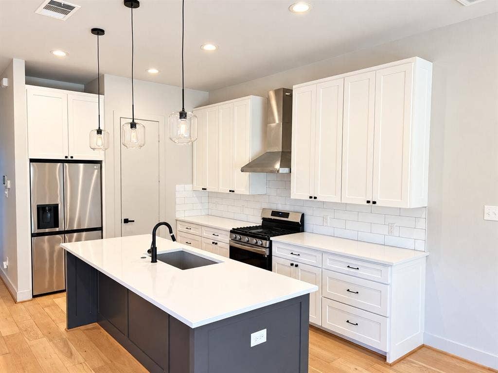 Kitchen featuring white shaker cabinetry, stainless steel appliances, a center island with a sink, white countertops, and wood-finish flooring