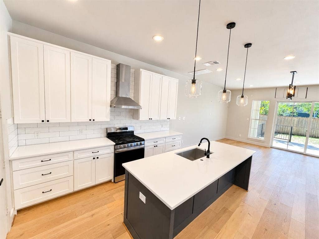 Modern kitchen featuring white shaker cabinetry, stainless steel gas range with hood ventilation, white subway tile backsplash, and quartz countertops