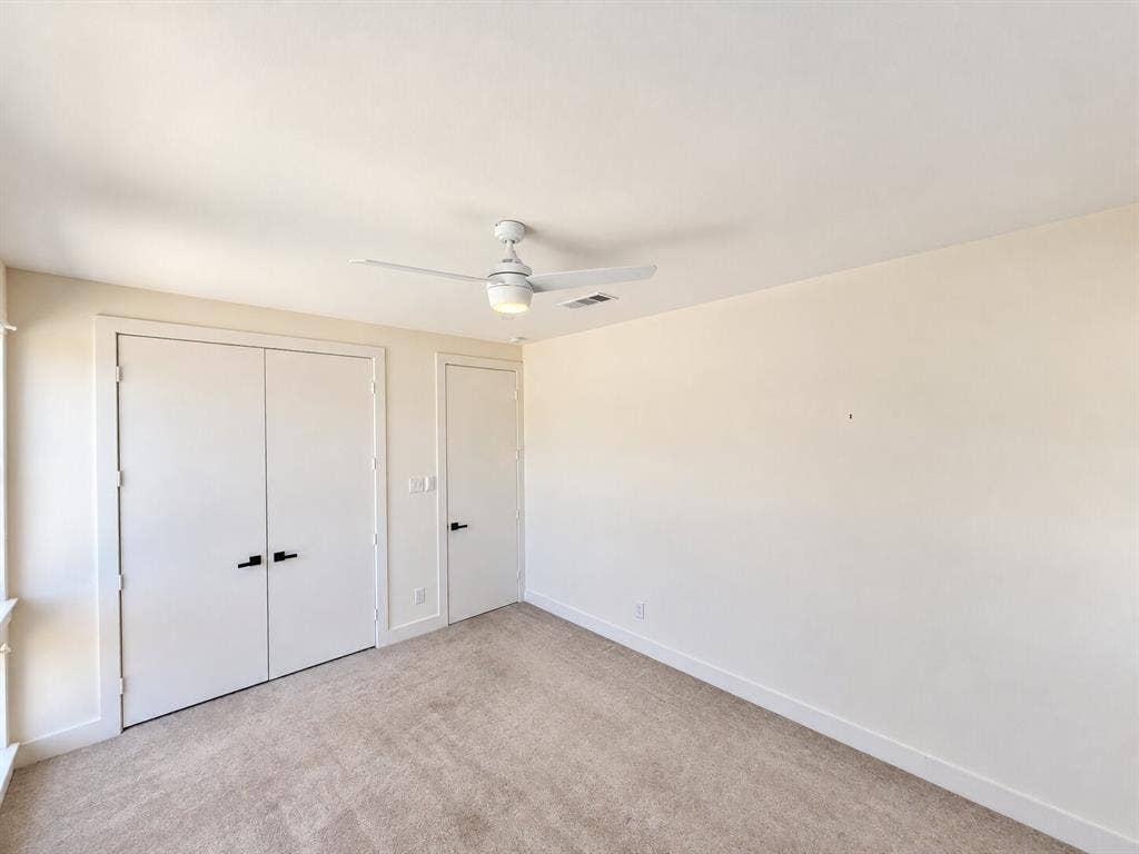 Beige carpeted flooring, white ceiling, white walls, white trim, matte black door hardware, ceiling fan with integrated lighting