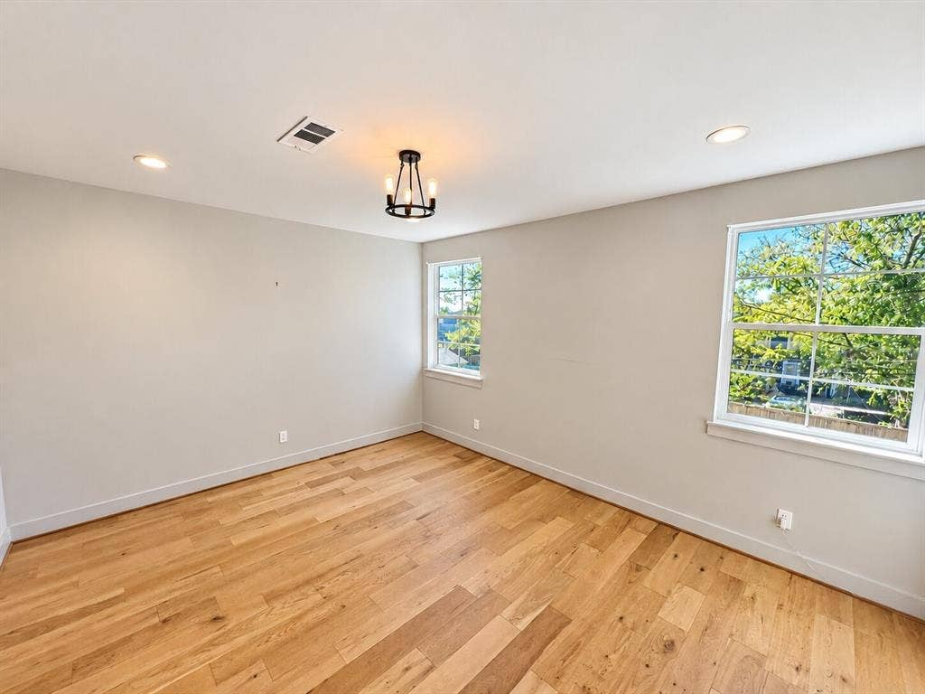 Hardwood flooring, two large windows, recessed lighting, and a modern chandelier