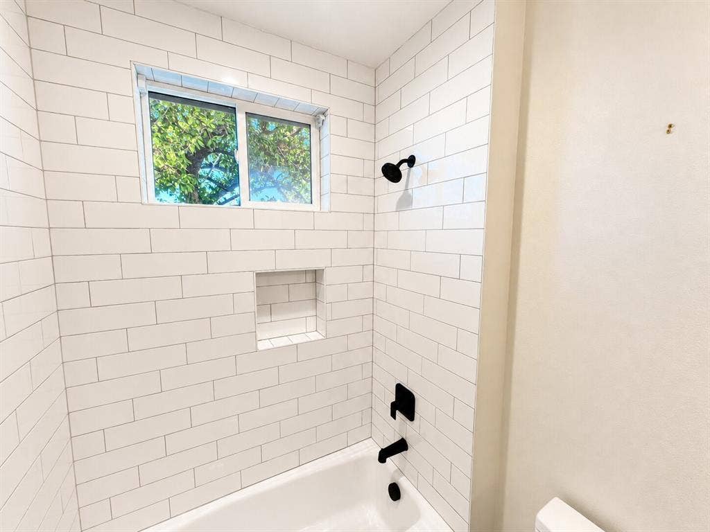 White subway tile shower surround featuring a built-in niche, black fixtures, and a white bathtub