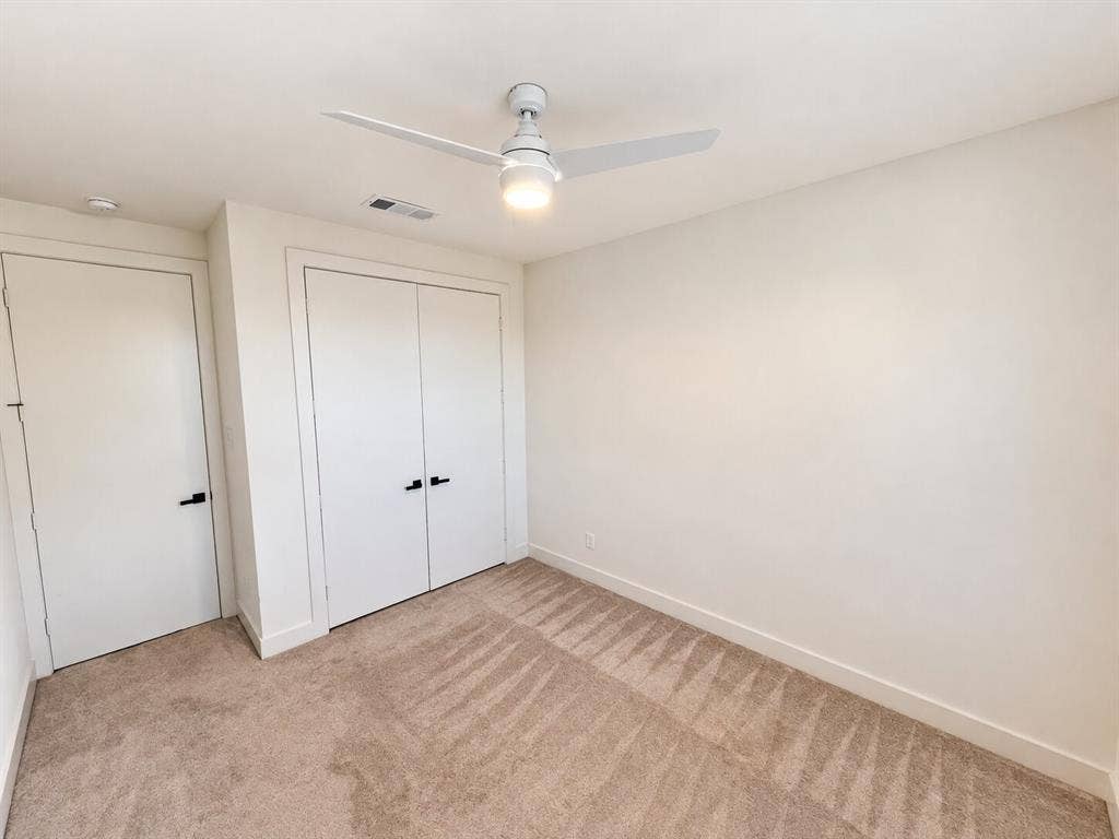 Neutral wall paint, ceiling fan with integrated lighting, two white panel doors, and carpet flooring