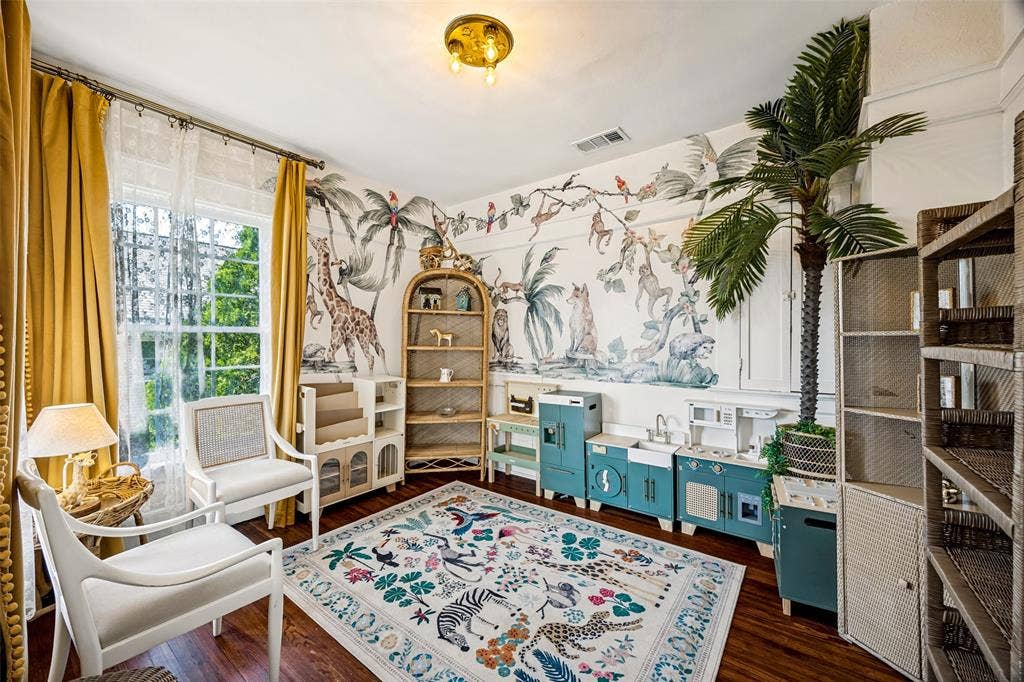 320 E 5th Street, Dallas, TX 75203 Bright corner study featuring hardwood flooring, custom built-in shelving with integrated storage, botanical wallcovering, large multi-pane windows with gold drapery hardware, and a brass ceiling fixture