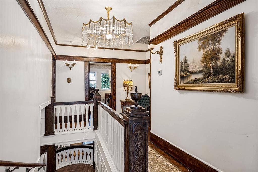 320 E 5th Street, Dallas, TX 75203 Ornate chandelier, dark wood trim, white balusters, and a decorative wall sconce