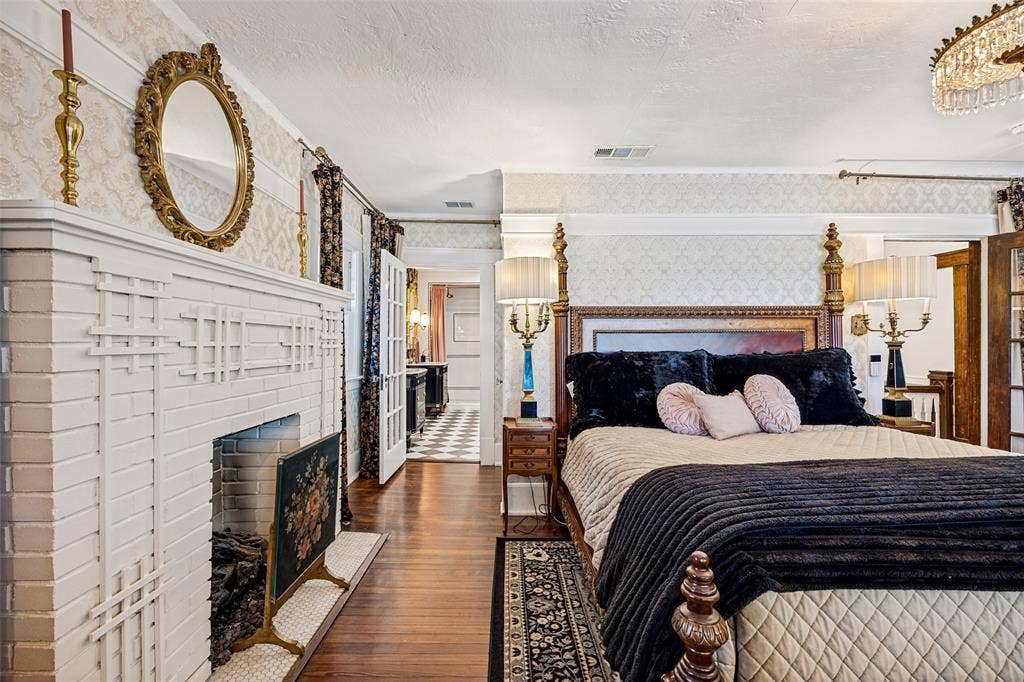320 E 5th Street, Dallas, TX 75203 Hardwood flooring, painted brick fireplace with decorative screen, patterned wallpaper, double French doors, and an ornate chandelier