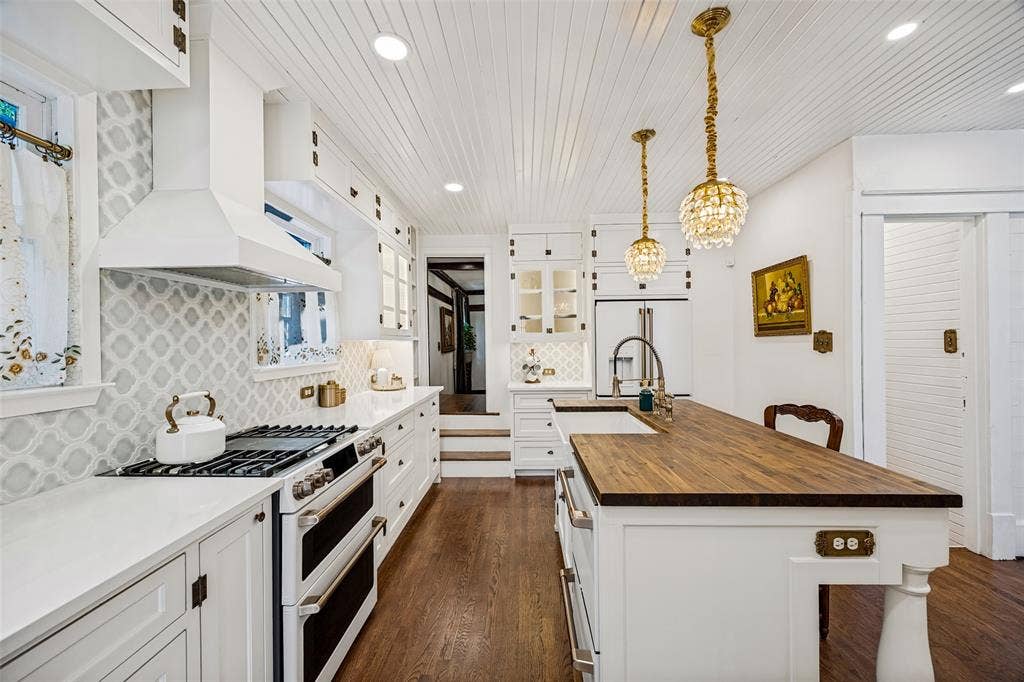320 E 5th Street, Dallas, TX 75203 White shaker cabinetry with dark hardware, full backsplash featuring patterned tiles, stainless steel range with double ovens, and a wood-finish island countertop