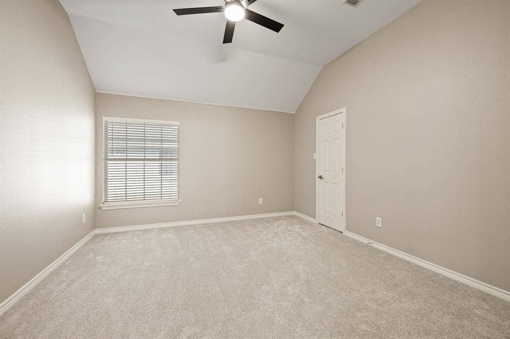 A comfortable secondary bedroom features a vaulted ceiling, neutral colors & a ceiling fan, ready for your personal touch.
