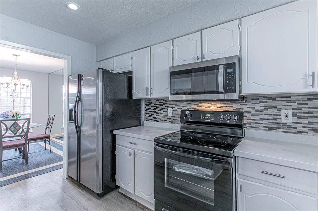 9326 Emberglow Lane, Dallas, TX 75243 Kitchen with appliances with stainless steel finishes, light wood-style flooring, backsplash, a chandelier, and a textured ceiling