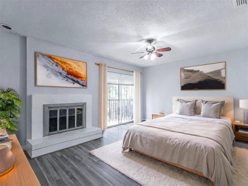 9326 Emberglow Lane, Dallas, TX 75243 Bedroom featuring a tiled fireplace, access to outside, wood finished floors, a textured ceiling, and a ceiling fan