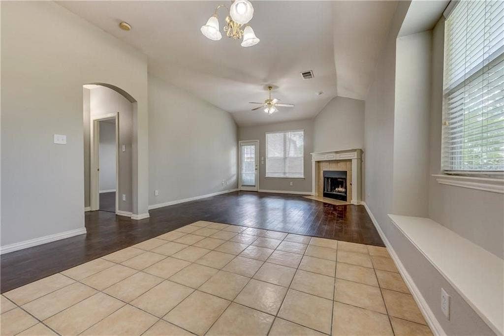 2300 Reston Drive, McKinney, TX 75072 Unfurnished living room featuring vaulted ceiling, ceiling fan with notable chandelier, and light tile floors