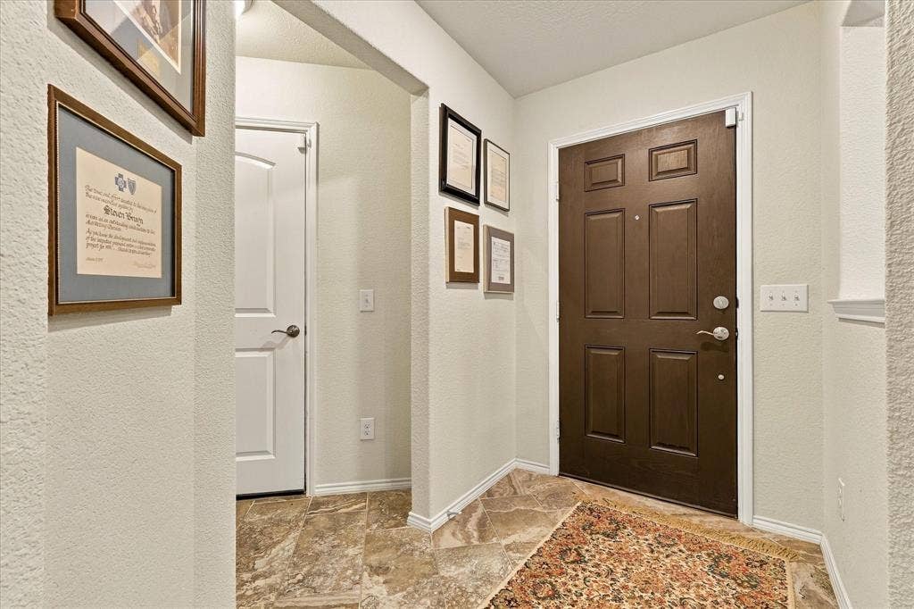 Entryway featuring a multi-panel door with metallic hardware, neutral wall paint, and stone-finish flooring