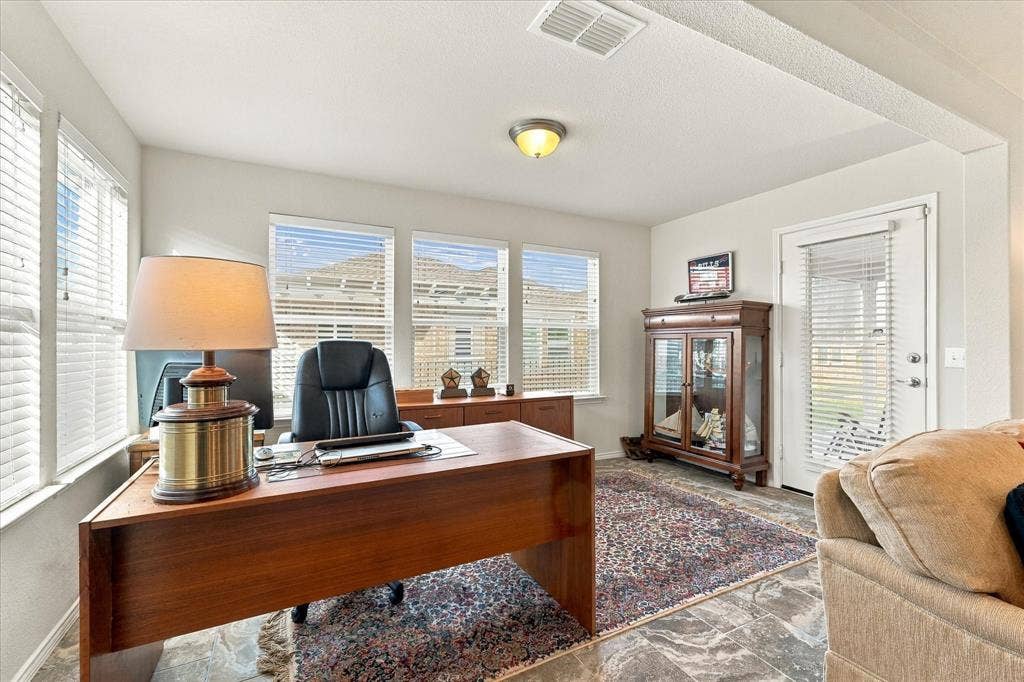 Neutral interior space featuring stone-style tile flooring, multiple windows with integrated blinds, and an exterior door with glass pane inset