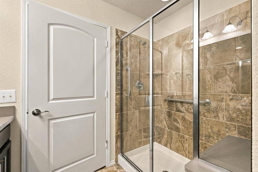 Walk-in shower featuring metallic-finish frame, stone-tile surround, integrated bench seating, and dual wall-mounted grab bars