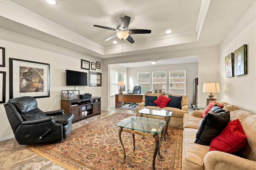 Tray ceiling with crown molding, central ceiling fan, recessed lighting, and expansive windows