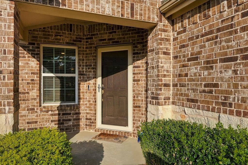 Exterior featuring a multi-toned brick facade, natural stone accents, covered entryway, and a paneled entry door