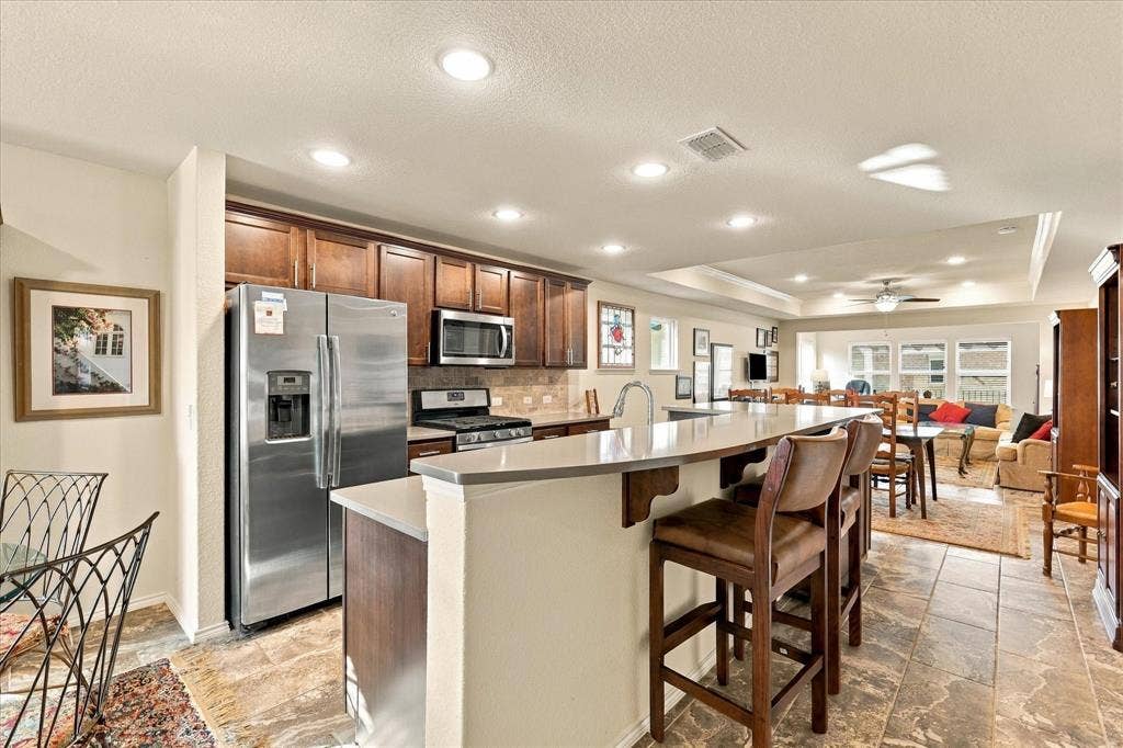 Kitchen featuring dark-finish wood cabinetry, stainless steel appliances, solid surface countertops with an integrated breakfast bar, and stone-tile flooring