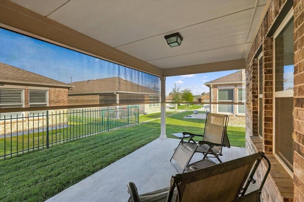 Covered patio featuring concrete flooring, a retractable mesh privacy screen, brick exterior wall, and mounted outdoor lighting