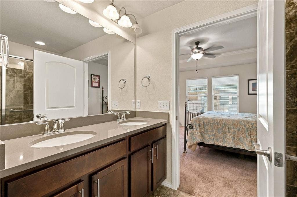 Ensuite Primary Bathroom featuring a dual-sink vanity with solid-surface countertops, wood-finish cabinetry, a full-width mirror, and chrome-finish fixtures