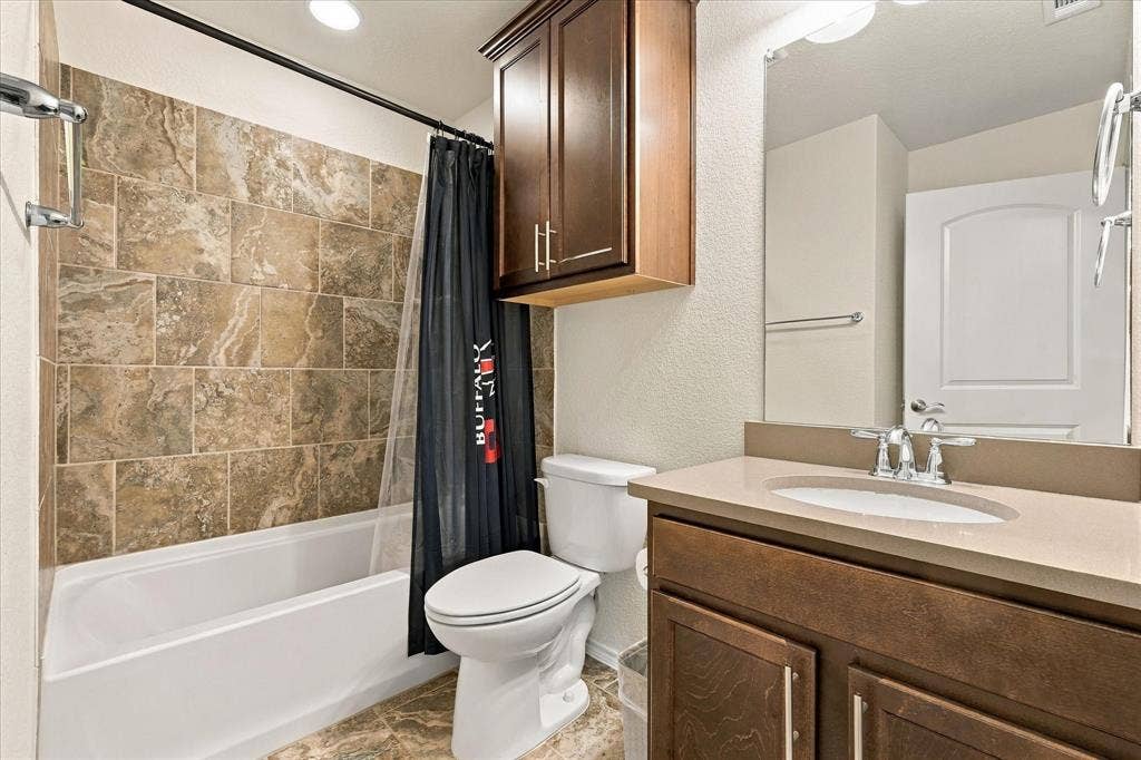 Bathroom featuring a vanity with a solid-surface countertop and integrated sink, custom wood cabinetry, a large wall-mounted mirror, and a shower-tub combination with tiled surround