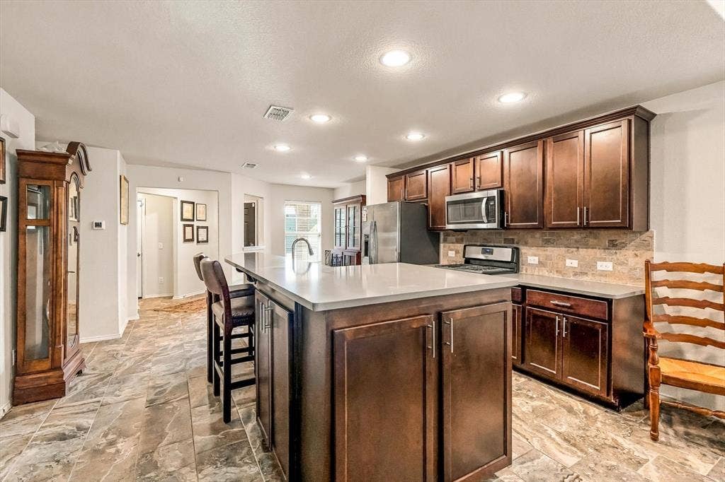Kitchen featuring dark wood cabinetry, a central island with a solid-surface countertop, stone-tile flooring, and recessed ceiling lighting