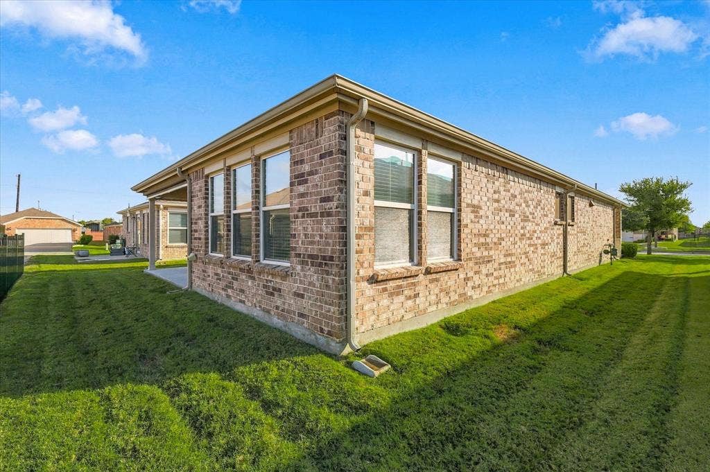 Full brick exterior featuring a covered patio, neutral-tone window frames, and surrounding lawn