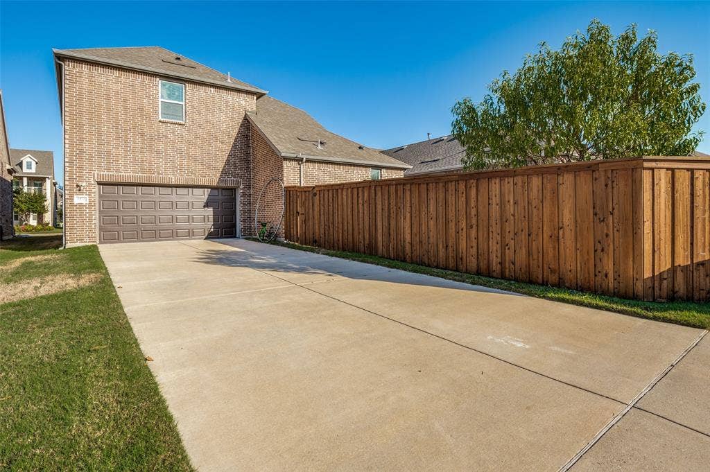 Two-story brick exterior featuring an attached two-car garage, concrete driveway, and full wood privacy fencing