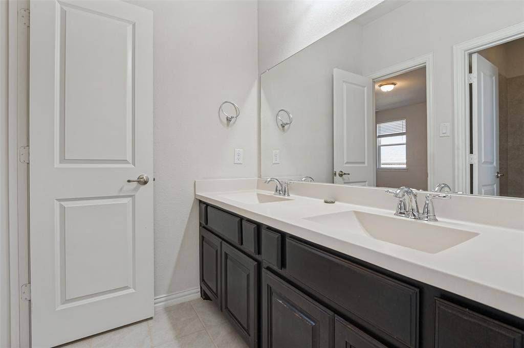 Dual-sink vanity with dark cabinetry, integrated solid-surface countertop, chrome hardware, and a wall-to-wall mirror