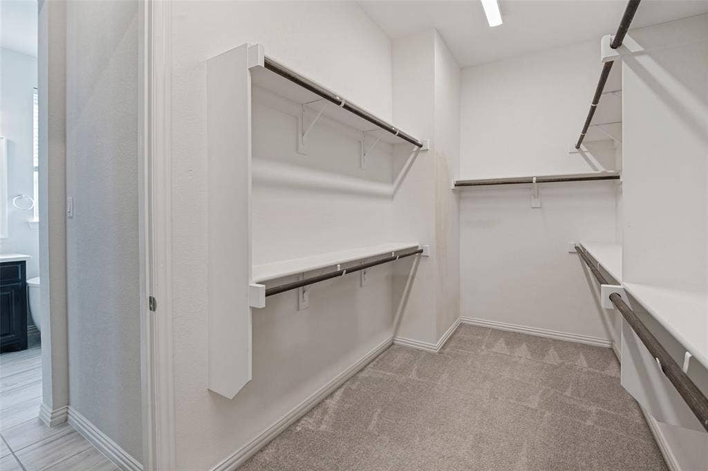 Walk-in closet featuring tiered shelving, integrated hanging rods, neutral carpeting, and overhead lighting