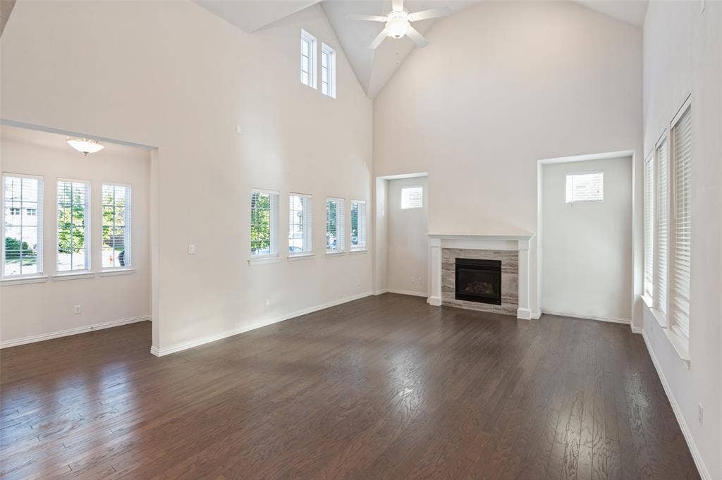 Vaulted ceilings featuring a central ceiling fan, wood-finish flooring, multi-pane windows, and a fireplace with a stone-surround mantel