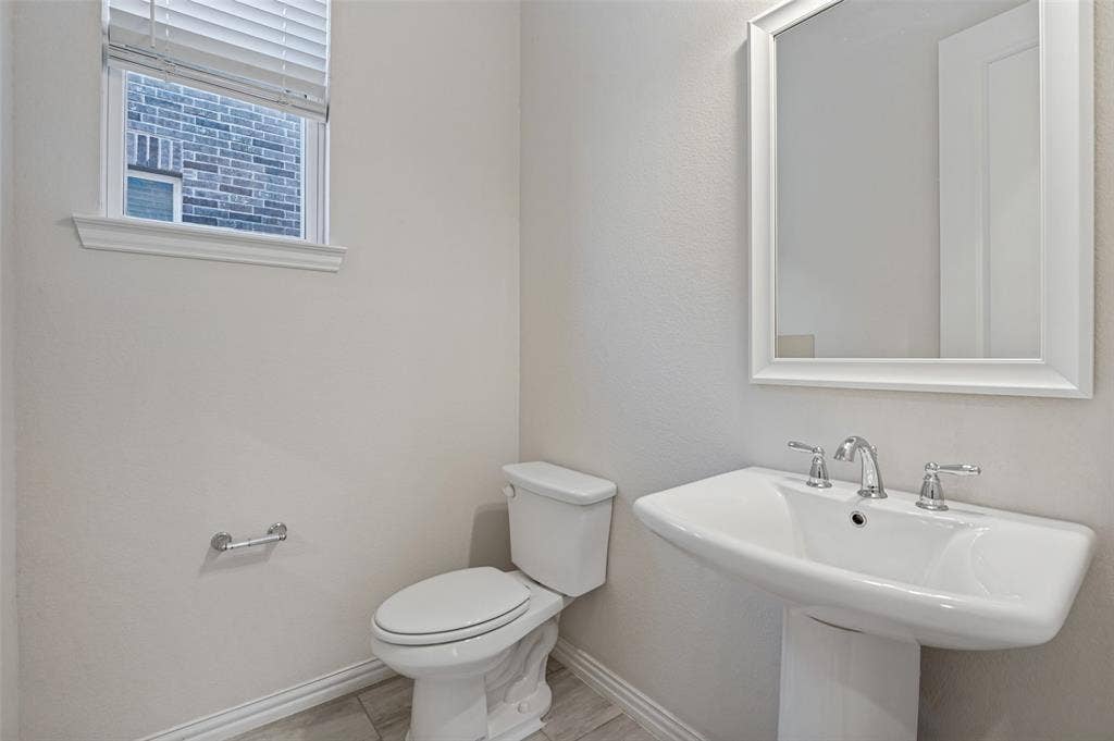 Pedestal sink with polished chrome widespread faucet, white framed mirror, dual-flush toilet, and wood-finish tile flooring