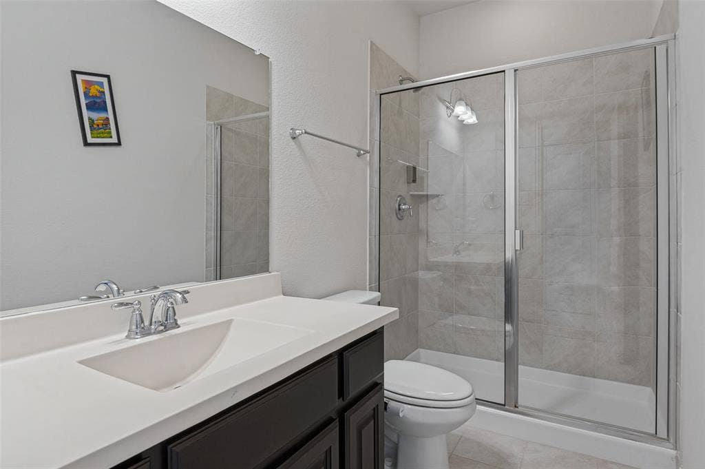 Bathroom featuring a dark-finish vanity with a seamless integrated sink, large wall-mounted mirror, and a walk-in shower with a glass enclosure and neutral-toned tile surround