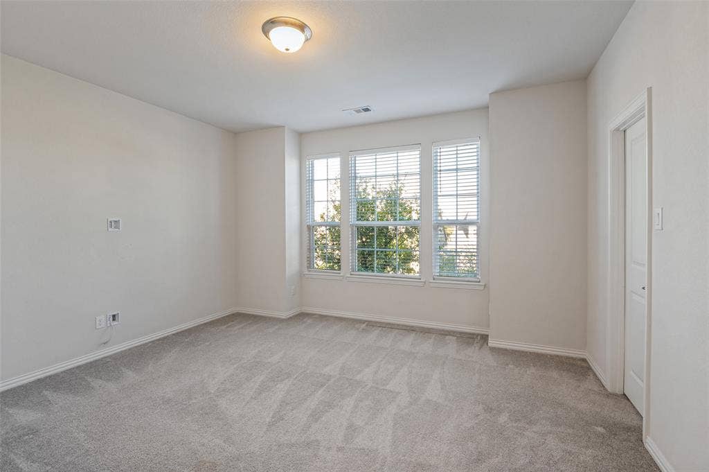 Neutral-toned wall paint, wall-to-wall carpeting, three-panel window configuration with horizontal blinds, and a flush-mount ceiling light fixture