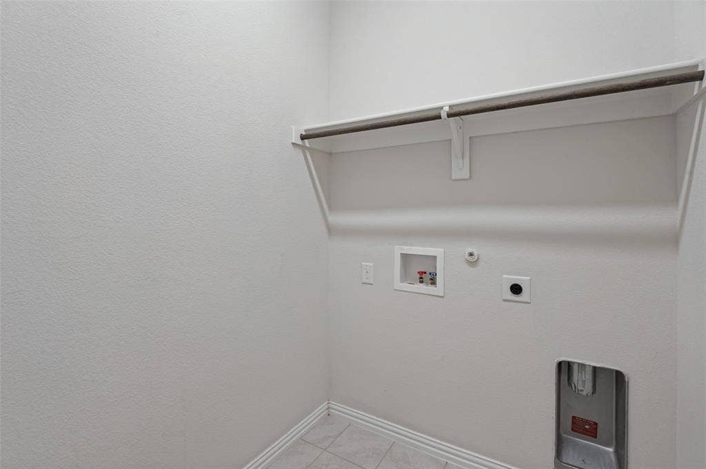Utility area featuring tile flooring, neutral wall paint, and a built-in shelf with a metal hanging rod