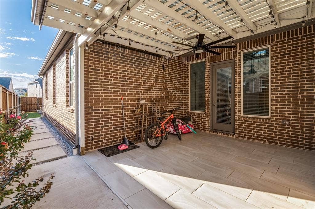 Covered patio featuring a brick exterior, large-format tile flooring, a slatted overhead pergola, and a ceiling-mounted fan