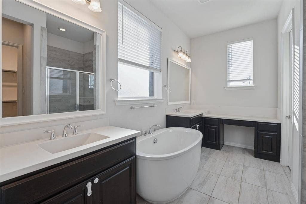 Bathroom featuring a freestanding oval soaking tub, dual dark-finish cabinetry with light countertops, rectangular undermount sinks, and light-tone tile flooring