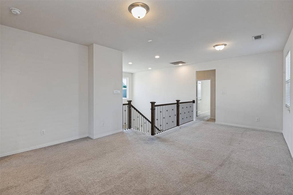 Open floor plan featuring neutral wall tones, carpeted flooring, recessed lighting, and a staircase with dark wood-finish railing and iron balusters